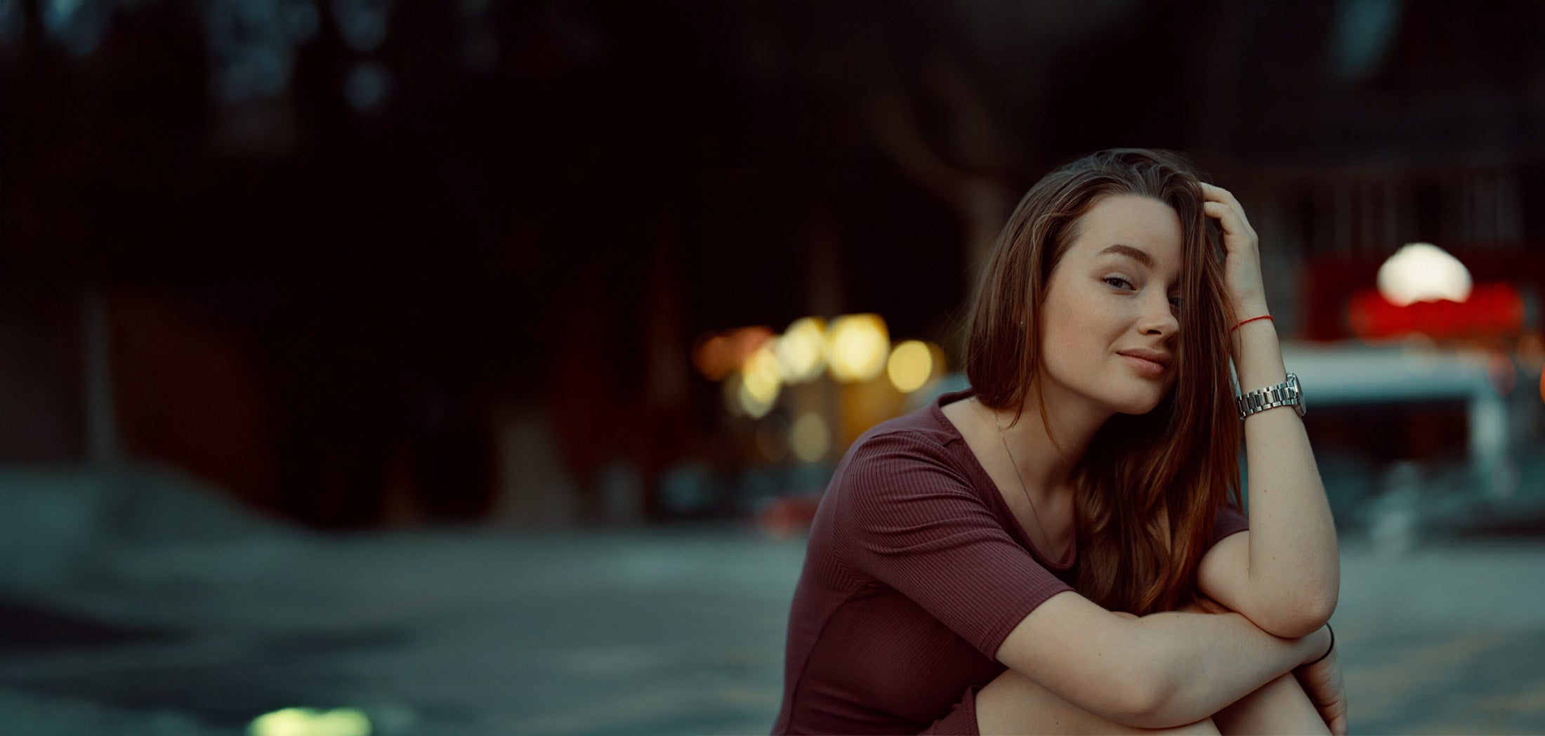 Young woman smiling sitting on curb of city at dusk